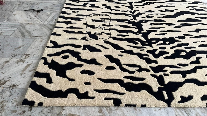 May include: A rectangular area rug featuring a high-contrast black and cream abstract pattern with organic, flowing shapes. The rug has a textured, tufted surface and includes a central logo stamp that reads House of Heritage Rugs.