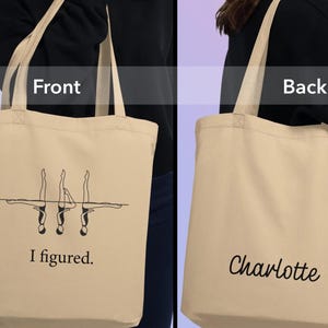Puede incluir: Bolso tote de lona beige con texto y gráficos negros. La parte delantera de la bolsa presenta un dibujo lineal de nadadoras sincronizadas y las palabras "I figured". La parte trasera de la bolsa tiene el nombre "Charlotte" en cursiva.
