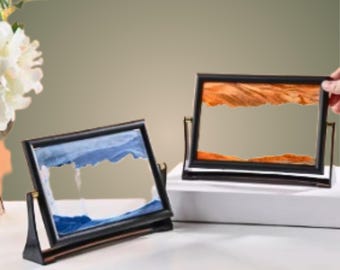 May include: Two sand art frames with black frames and a stand. The sand art in the left frame is blue and the sand art in the right frame is orange.