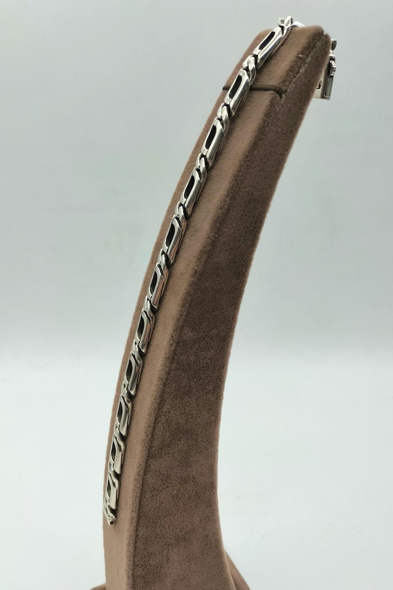 May include: A silver chain bracelet with a box chain design. The bracelet is displayed on a brown velvet stand.