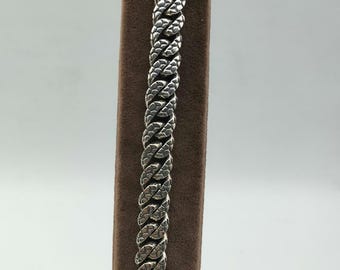 May include: A silver chain bracelet with a textured, diamond-cut design. The bracelet is displayed on a brown velvet background.