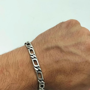 May include: A silver chain bracelet with a curb link design. The bracelet is on a person's wrist.