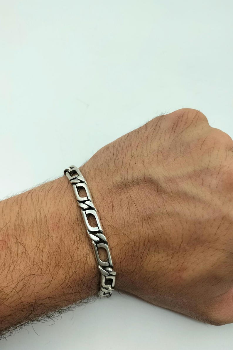 May include: A silver chain bracelet with a curb link design. The bracelet is on a person's wrist.