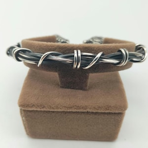 May include: A silver and black barbed wire bracelet on a brown velvet display box.
