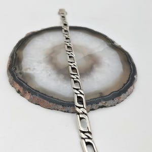 May include: A silver chain bracelet with a box clasp. The bracelet is on a white agate background.
