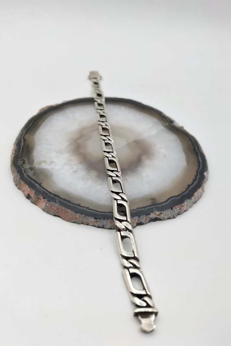 May include: A silver chain bracelet with a box clasp. The bracelet is on a white agate background.