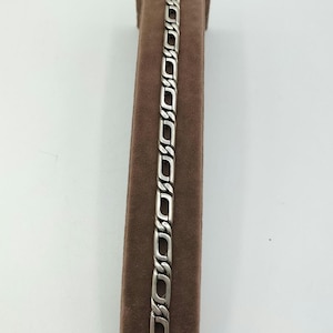 May include: A silver chain bracelet with a box clasp. The bracelet is displayed on a brown velvet stand.