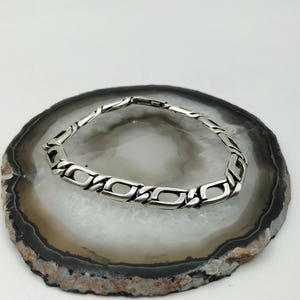 May include: A silver chain bracelet with a box chain design. The bracelet is on a white and brown agate slice.