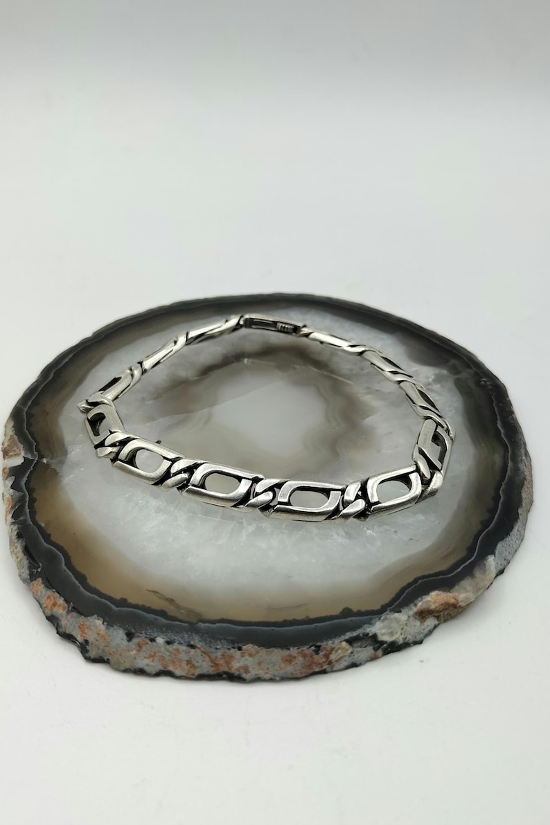 May include: A silver chain bracelet with a box chain design. The bracelet is on a white and brown agate slice.