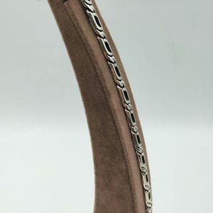 May include: A silver chain bracelet with a braided design. The bracelet is displayed on a brown velvet stand.