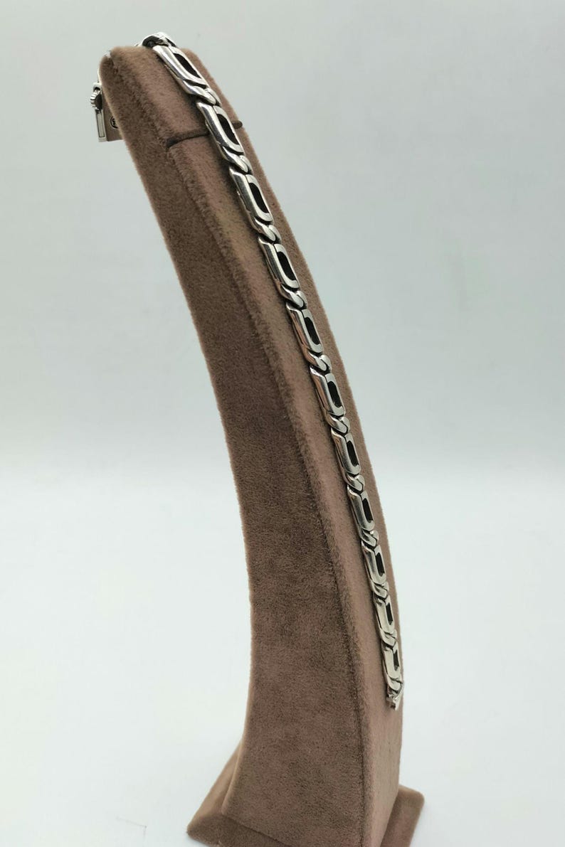 May include: A silver chain bracelet with a braided design. The bracelet is displayed on a brown velvet stand.