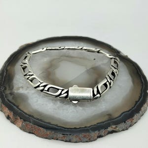 May include: A silver chain bracelet with a box clasp closure. The bracelet is on a white and gray agate slice.