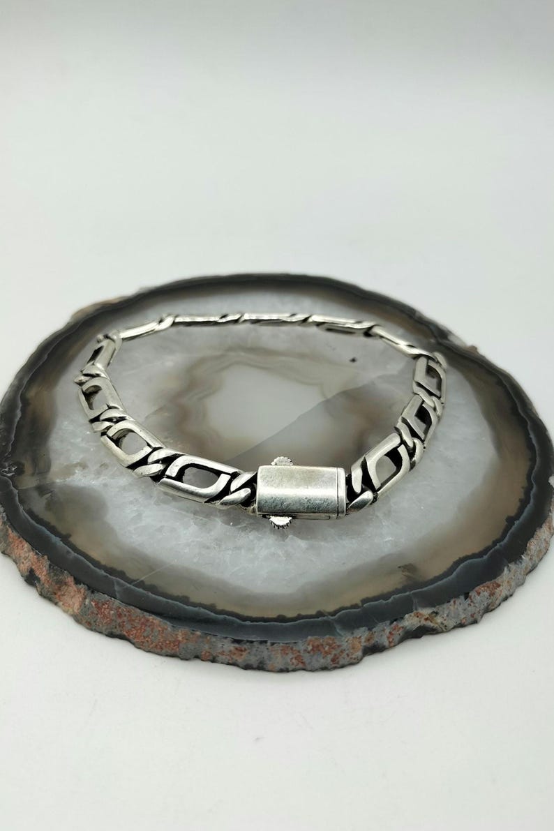 May include: A silver chain bracelet with a box clasp closure. The bracelet is on a white and gray agate slice.