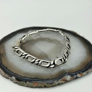 May include: A silver chain bracelet with a box clasp. The bracelet is on a white and gray agate slice.