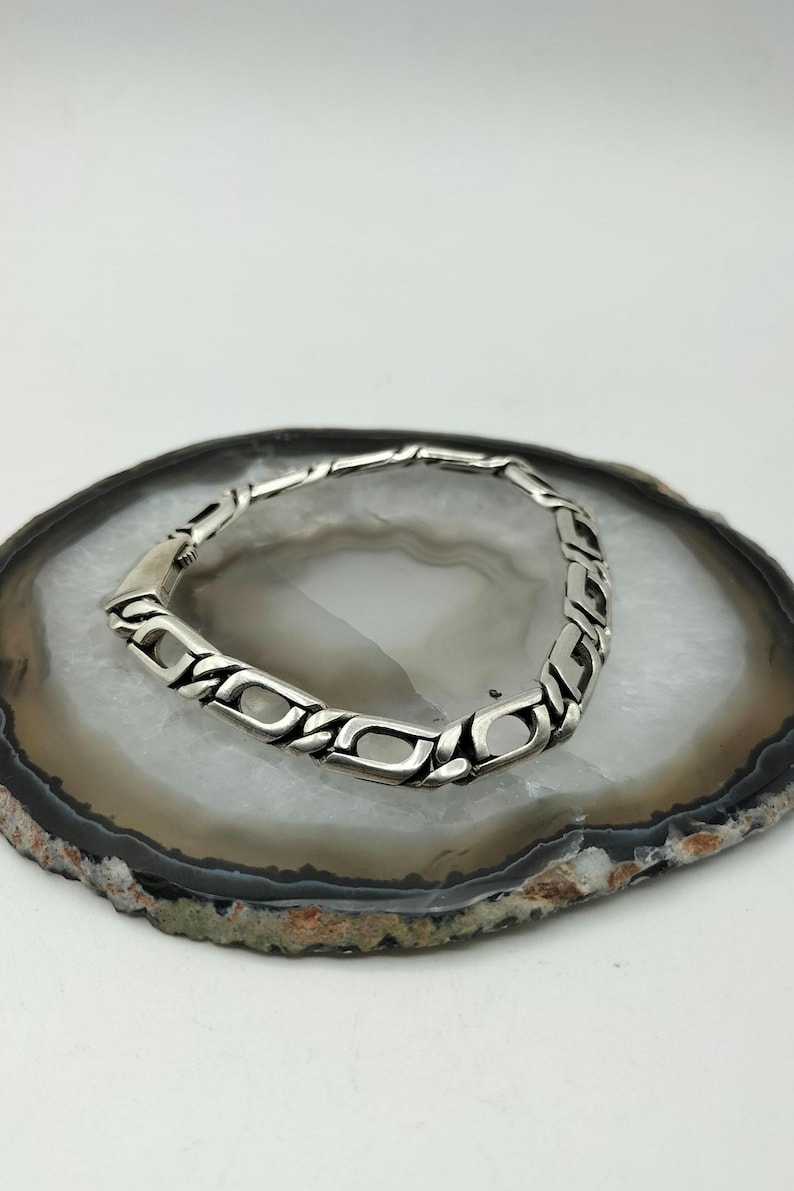 May include: A silver chain bracelet with a box clasp. The bracelet is on a white and gray agate slice.