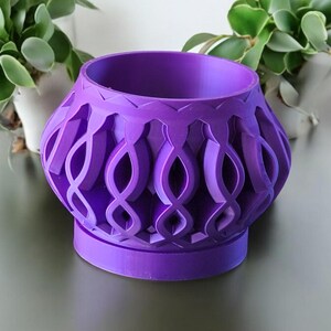 Peut inclure: Pot de fleurs violet avec un design décoratif et complexe. Le pot a une large ouverture ronde et une base ronde plus petite.