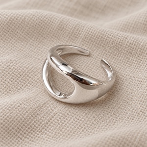 May include: A polished silver-tone open ring featuring a smooth, rounded band that curves to create a central negative space. The ring has an adjustable open back design with tapered ends, showcasing a reflective metallic finish throughout.