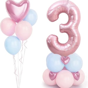 May include: A pink number 3 balloon with a pink heart balloon on top. The number balloon is surrounded by pink and blue balloons.