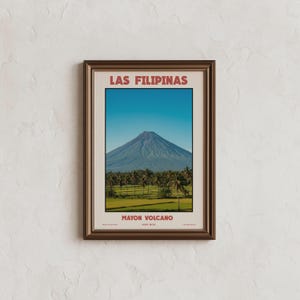 May include: Framed print featuring a landscape of the Mayon Volcano in the Philippines. The image shows a symmetrical view of the volcano under a clear blue sky, with palm trees and green fields in the foreground. The text "LAS FILIPINAS" and "MAYON VOLCANO" are printed in red.