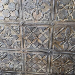 May include: Close-up of a wooden surface with a repeating pattern of carved floral and geometric designs. The designs are in a lighter color than the wood, creating a contrast. The wood has a natural, aged appearance.