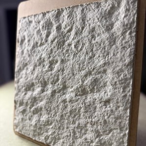 Puede incluir: Primer plano de un panel de pared de piedra artificial texturizado blanco. El panel está montado en un marco de madera.