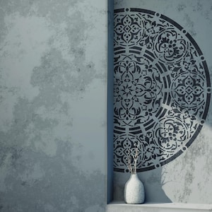 May include: A decorative wall stencil featuring a half-circle design with intricate, symmetrical patterns in black. The stencil is applied to a textured, light gray wall. A small, white vase with dried branches sits below the stencil.