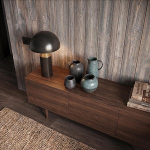 May include: A dark mushroom-shaped table lamp with a gold base, a collection of four ceramic vessels in shades of blue and charcoal, and a stack of books with visible text on the spines, all arranged on a dark wood console table.