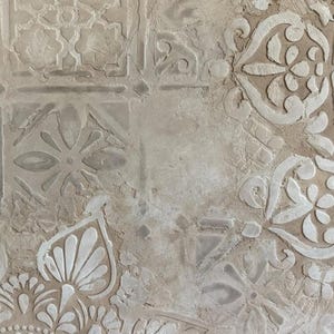 May include: Close-up of a textured, beige surface with a repeating pattern of raised white floral and geometric designs. The design elements include stylized flowers, leaves, and geometric shapes, creating a decorative, vintage aesthetic.