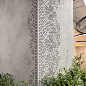 May include: A light gray wall featuring a vertical decorative panel with a dark gray geometric pattern. The design consists of repeating star-like shapes and intricate diamond motifs arranged in a symmetrical column against a textured surface.