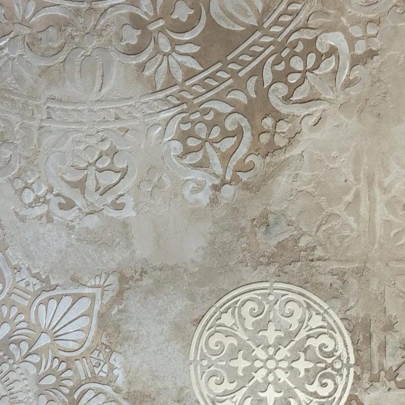 May include: A textured, beige-toned surface with a repeating pattern of white, ornate floral and geometric designs. The design elements include circular and semi-circular shapes, with a distressed, aged appearance.