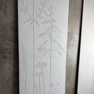 Peut inclure: Une &oelig;uvre d'art murale rectangulaire, blanc cass&eacute;, avec un motif botanique en relief. L'&oelig;uvre repr&eacute;sente diverses plantes, notamment de hautes tiges avec des feuilles et des fleurs. Le relief cr&eacute;e un effet textur&eacute; en trois dimensions.