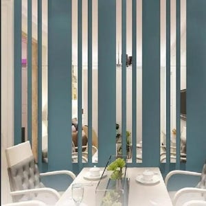 Può includere: Un divisorio per ambienti color teal con doghe verticali, che crea un'estetica moderna. Il divisorio separa una zona pranzo con un tavolo bianco, sedie e un centrotavola in vetro. Il design permette il passaggio della luce, esaltando l'apertura.