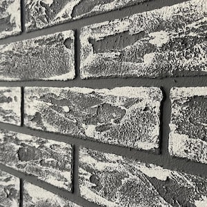 Puede incluir: Primer plano de una pared de ladrillos con superficie texturizada. Los ladrillos son de color gris oscuro con detalles en blanco, y el mortero es de un gris más oscuro. La pared tiene un aspecto rústico y desgastado.