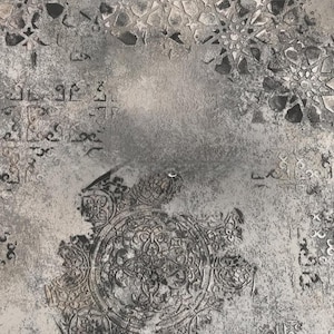 Puede incluir: Fondo gris texturizado con patrones florales y geométricos en relieve. El diseño presenta escritura árabe descolorida y motivos circulares ornamentados, creando una apariencia vintage y desgastada. La estética general recuerda a la piedra o yeso envejecido.