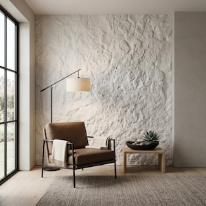 May include: A modern living room scene featuring a brown leather armchair with a black metal frame, a beige throw blanket, and a floor lamp with a beige lampshade. The room has a textured white stone wall and a small wooden side table.