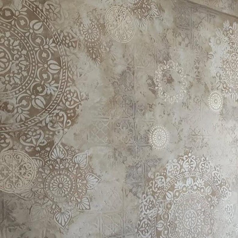 May include: A wall with a textured, aged appearance. The surface is primarily beige with intricate, repeating patterns in a lighter, off-white color. The design features circular and floral motifs, creating a vintage or bohemian aesthetic.