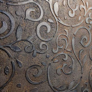May include: Close-up of a textured, brown surface with a repeating pattern of stylized, swirling floral designs. The raised elements of the pattern are a darker, metallic gray, creating a contrast with the background.