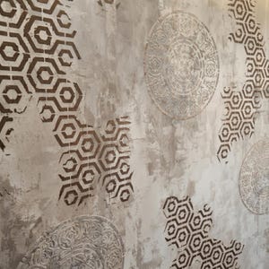 May include: Textured wall with a distressed, neutral color palette. The design features repeating geometric patterns in a dark brown color, along with circular, ornate, raised designs. The overall aesthetic is rustic and artistic.