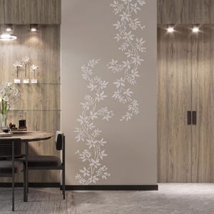 May include: A vertical wall decal featuring a white floral vine pattern with delicate leaves and blossoms. The design is applied to a smooth, light-colored wall surface, creating a continuous botanical motif that extends from the floor upward.