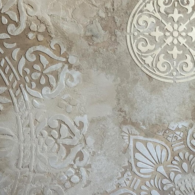 May include: Close-up of a textured wall with a distressed, aged appearance. The wall features a mix of beige and brown tones with white, raised, ornate floral and geometric patterns. The design evokes a vintage or antique aesthetic.