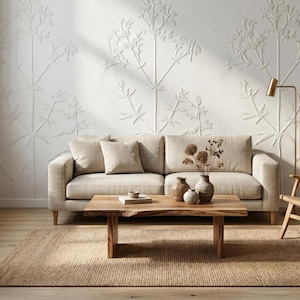 May include: A living room scene featuring a beige sofa with throw pillows, a wooden coffee table, and a woven rug. The wall is decorated with a white floral pattern, and a gold floor lamp stands nearby. Decorative vases with dried flowers are on the table.