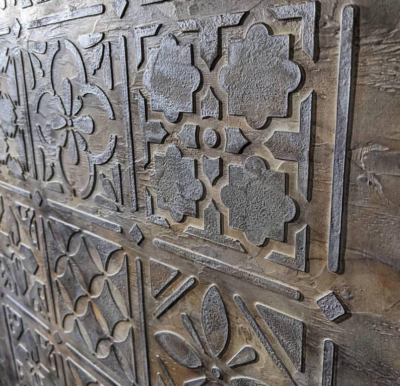 May include: Close-up of a decorative wooden panel with a repeating pattern of carved floral and geometric designs. The panel has a weathered, textured appearance with shades of brown and gray, creating a rustic aesthetic.