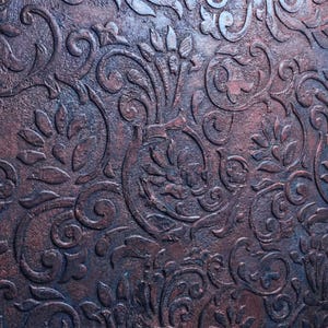 May include: Close-up of a textured surface with a repeating embossed floral pattern. The design features swirling leaves and stylized flowers in shades of brown and dark blue, creating a vintage aesthetic.