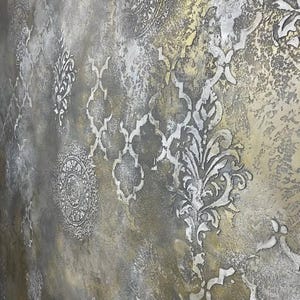 May include: Textured wall art with a distressed metallic finish. The design features repeating patterns of ornate floral and geometric shapes in silver and gold tones, creating a vintage aesthetic.