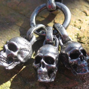 Puede incluir: Un collar de cadena de plata con tres dijes de calavera de plata. Las calaveras son detalladas y tienen un aspecto realista.