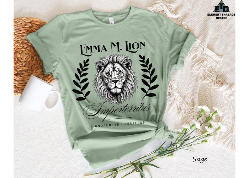 A green t-shirt with a lion graphic and text, along with a mug and some flowers, is displayed on a white surface.