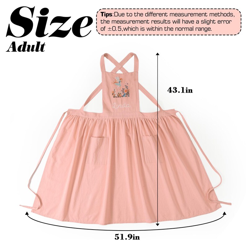 May include: A pink adult apron featuring a floral and fairy graphic with the name "Lynda" embroidered on the chest. The apron has cross-back straps and two front pockets. Dimensions are 109.47 cm in length and 131.83 cm in width.