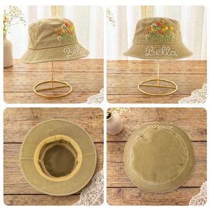 May include: A tan bucket hat featuring embroidered colorful wildflowers and the name Bella stitched in white cursive thread. The hat has a wide brim and a structured crown, shown from multiple angles including the interior and top view.