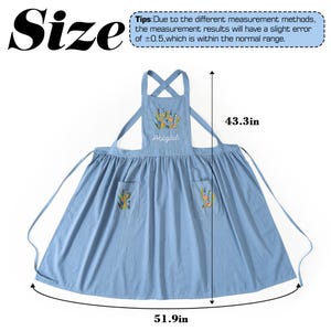 May include: A light blue apron featuring floral embroidery on the chest and two front pockets. The name Abigail is embroidered in white script on the chest. The apron measures 43.3 inches in length and 51.9 inches in width as indicated by arrows.