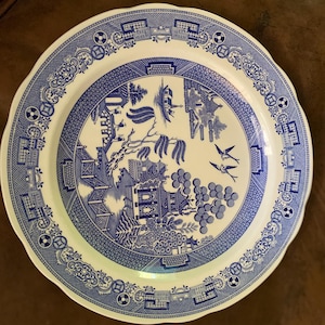 May include: A blue and white ceramic dinner plate featuring a willow pattern design. The plate has a scalloped edge and a white background with a blue border.